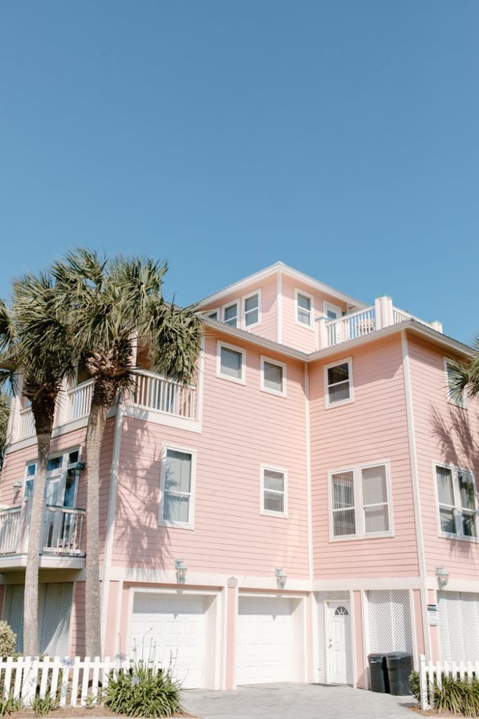 A pastel pink beach house with palm trees against a clear blue sky, perfect for coastal living themes.